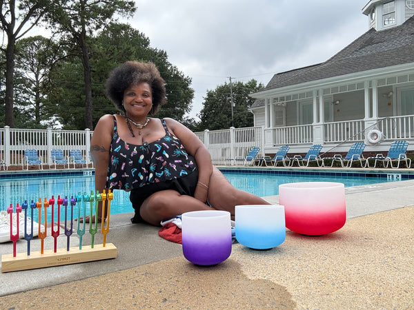 Beautiful African Indian American Woman sitting by a pool with colorful gradient candles, crystal bowls, and tuning forks. Queenin Telena Banks